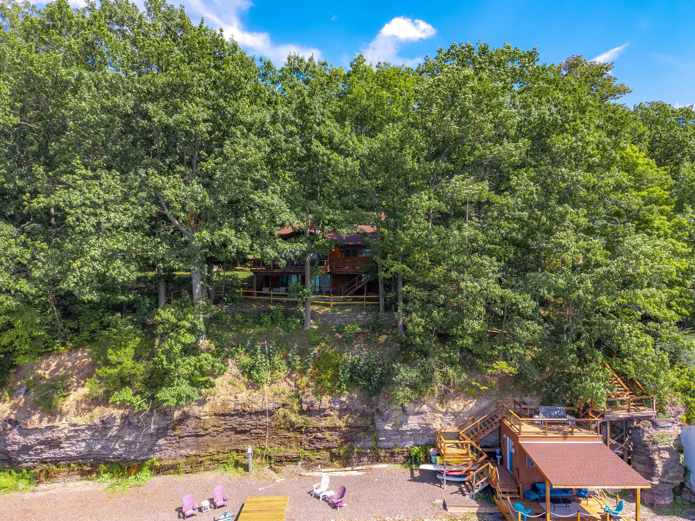 Lakeside Landing FLX from the water — main house on the bluff, deck level below, boathouse at the shale beach